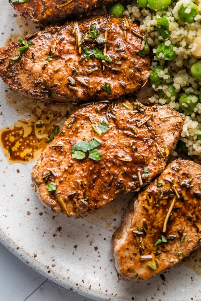 Close up of pork tenderloin medallions pan-seared in a simple homemade balsamic pan sauce, garnished with fresh parsley, and plated with a couscous and pea salad.