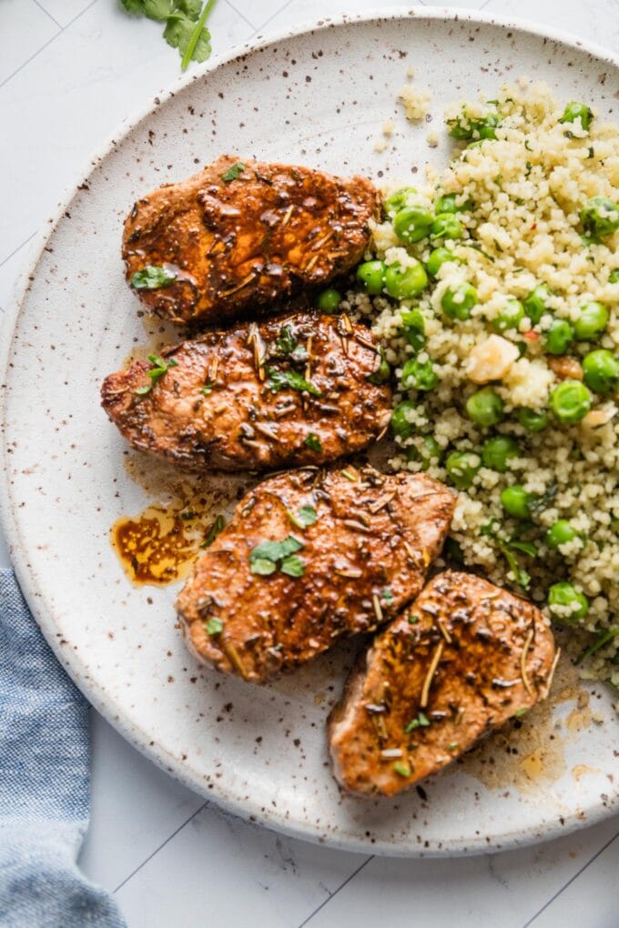 Dinner plate with pork tenderloin medallions in a balsamic pan sauce, fresh herbs, and a couscous salad with peas and walnuts.