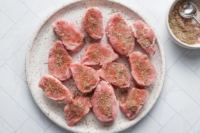 Large white plate filled with uncooked pork medallions seasoned with a homemade spice rub.