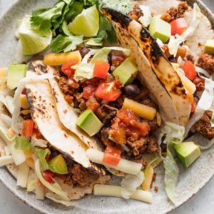 Overhead view of a plate with three ground beef and bean tacos in soft flour tortillas.