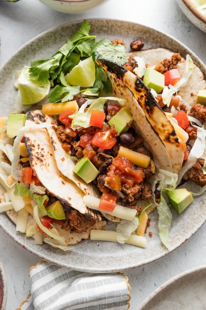 Overhead view of a plate with three ground beef and bean tacos in soft flour tortillas.