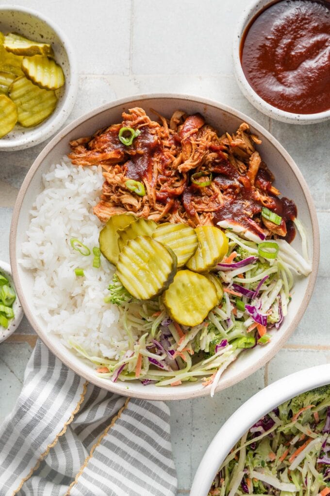 Low bowl filled with pulled BBQ chicken, rice, pickles, and coleslaw.