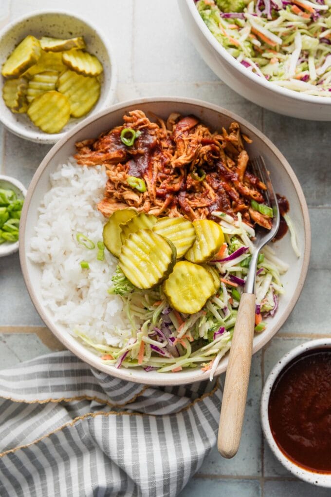 Counter set with bowls of pulled BBQ chicken with rice and slaw.