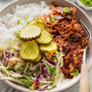Close up of a pulled BBQ chicken bowl with rice, coleslaw, and pickles.