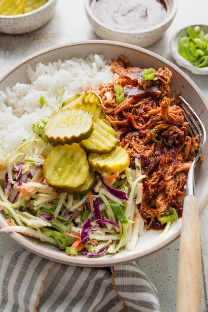 Close up of a pulled BBQ chicken bowl with rice, coleslaw, and pickles.