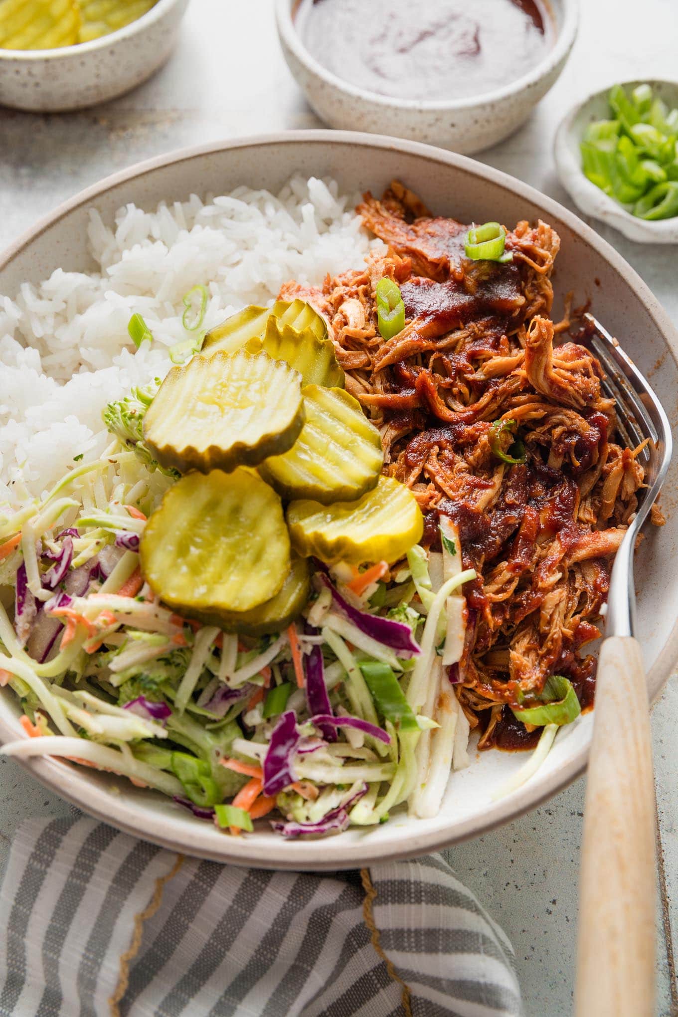 Close up of a pulled BBQ chicken bowl with rice, coleslaw, and pickles.