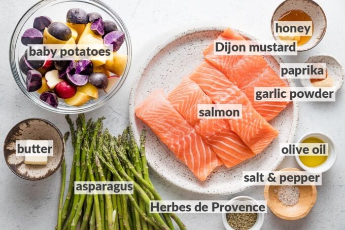Labeled overhead photo of salmon filets, quartered baby potatoes, asparagus spears, butter, olive oil, and seasonings.