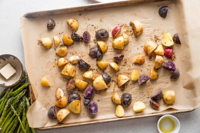 Multi-colored quartered baby potatoes seasoned and spread out on a rimmed parchment-lined sheet pan.