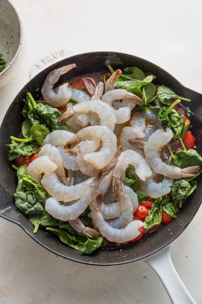 Raw shrimp and baby spinach added to light sauce in a cast iron skillet.