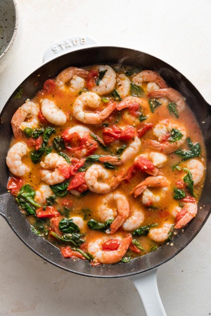 Simmered sauce with cooked shrimp, tomatoes, and spinach.