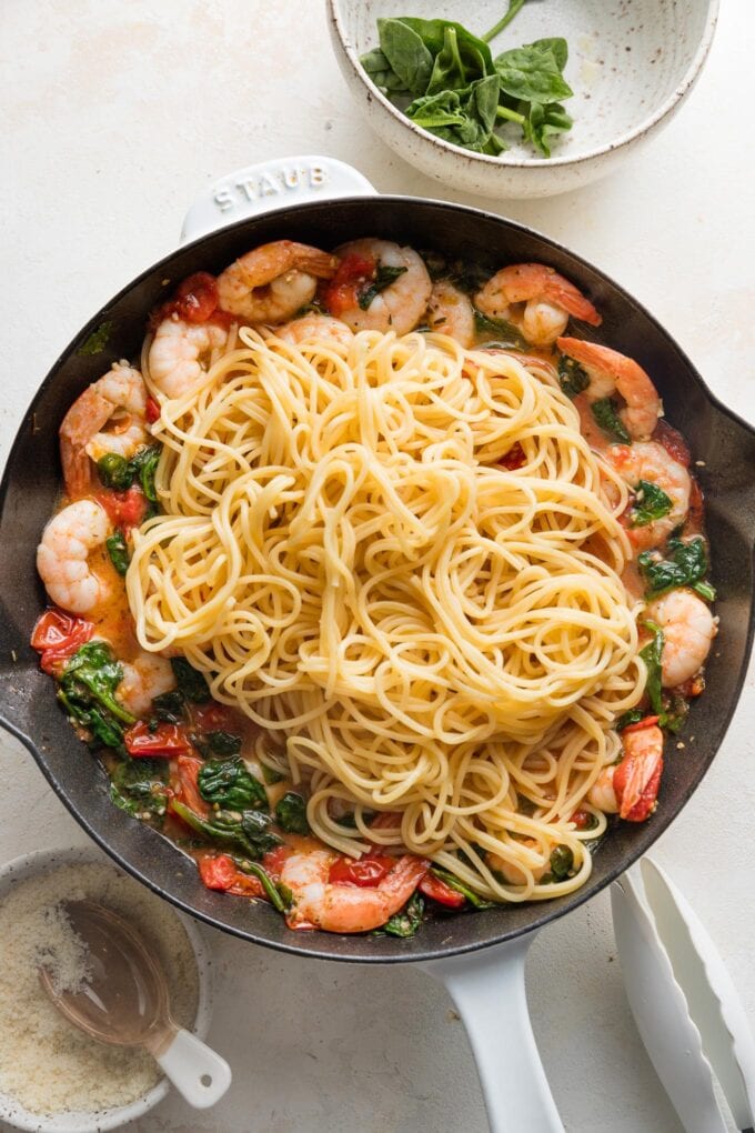 Cooked spaghetti added to tomato spinach sauce in a skillet.