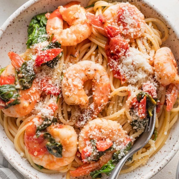 Bowl of tomato spinach shrimp pasta garnished with grated Parmesan cheese.