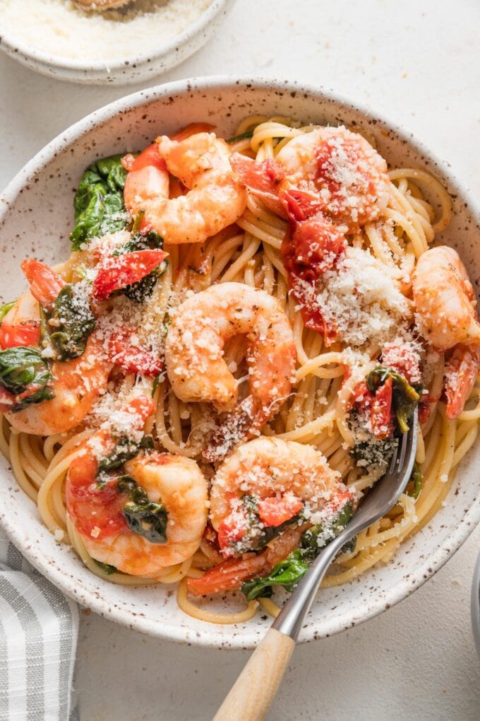 Bowl of tomato spinach shrimp pasta garnished with grated Parmesan cheese.