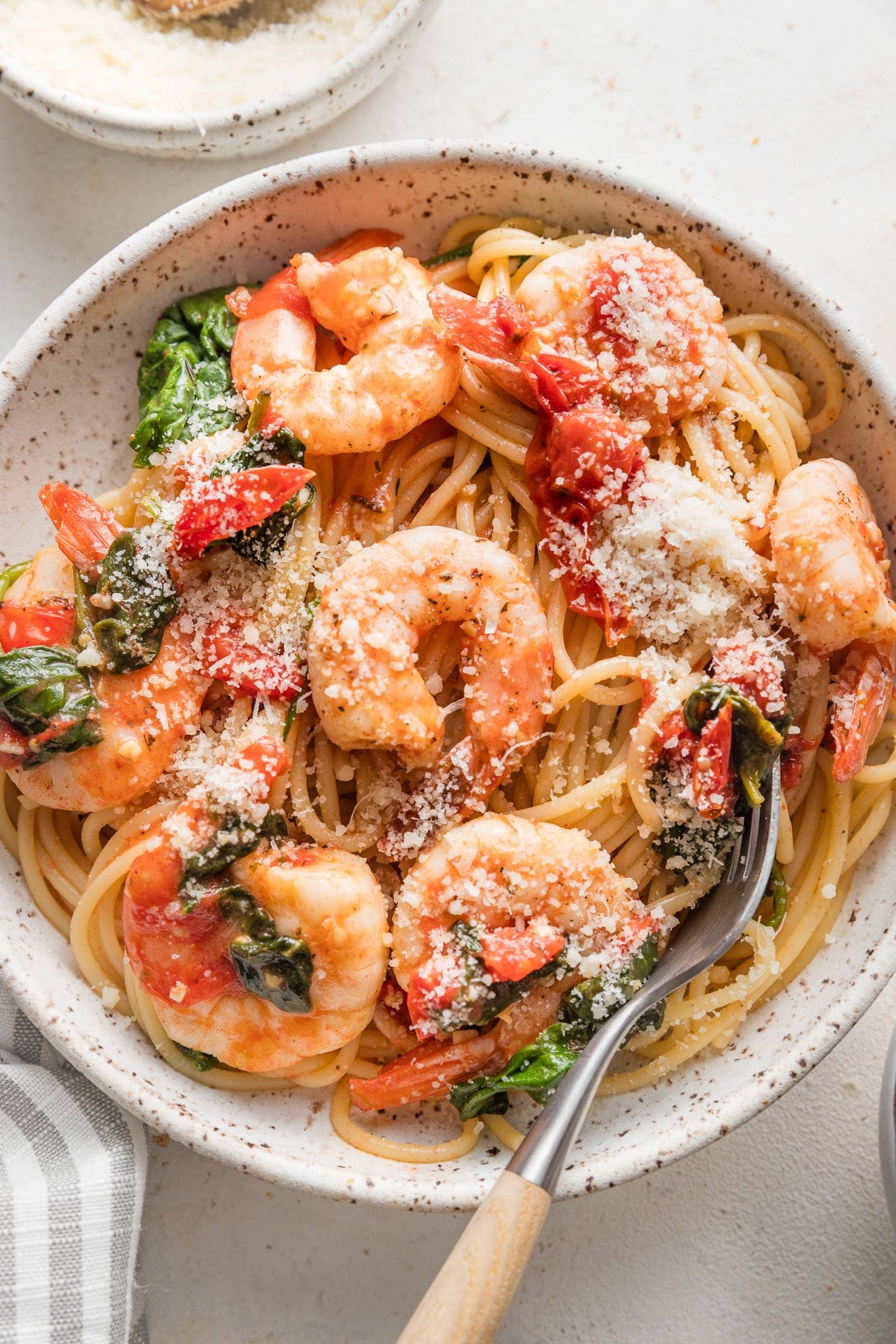 Bowl of tomato spinach shrimp pasta garnished with grated Parmesan cheese.