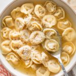 Shallow bowl full of tortellini simmered in bone broth and garnished with fresh cracked black pepper and grated Parmesan cheese.