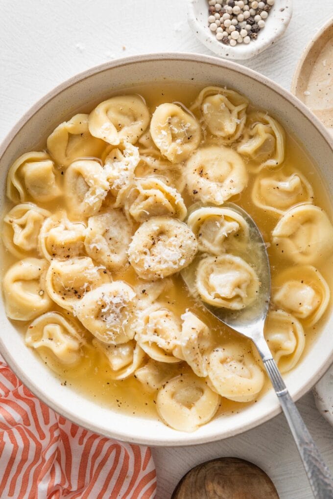 Shallow bowl full of tortellini simmered in bone broth and garnished with fresh cracked black pepper and grated Parmesan cheese.
