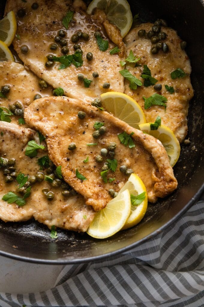Close up of a chicken breast in piccata sauce in a black cast iron skillet.