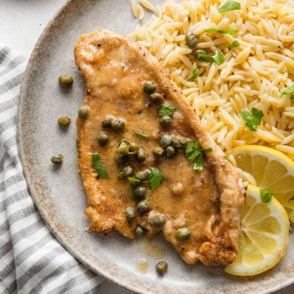 Small plate with a helping of buttered orzo and quick chicken piccata with extra lemon and capers.