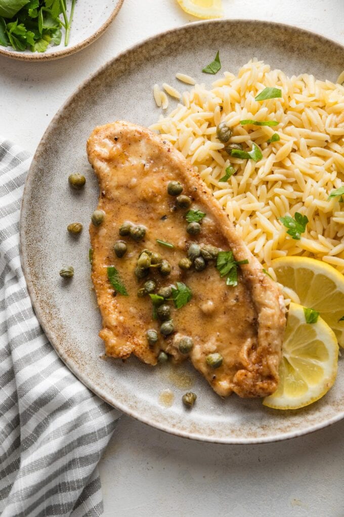 Small plate with a helping of buttered orzo and quick chicken piccata with extra lemon and capers.