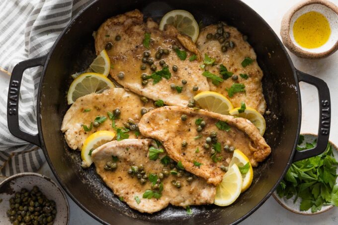 Large, deep-sided cast iron skillet filled with lemon chicken piccata garnished with extra lemon slices and fresh parsley.