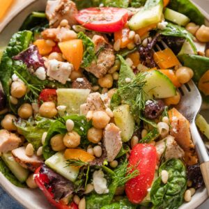 Bowl full of a chopped Mediterranean-style salad with greens, veggies, olives, and grilled chicken.