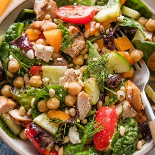Bowl full of a chopped Mediterranean-style salad with greens, veggies, olives, and grilled chicken.