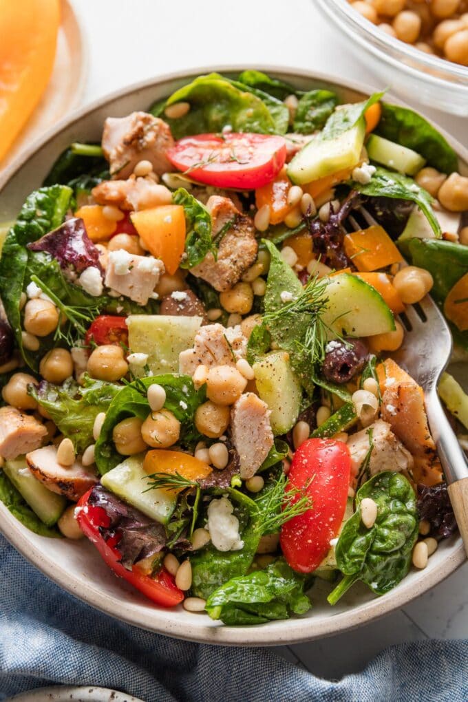 Bowl full of a chopped Mediterranean-style salad with greens, veggies, olives, and grilled chicken.