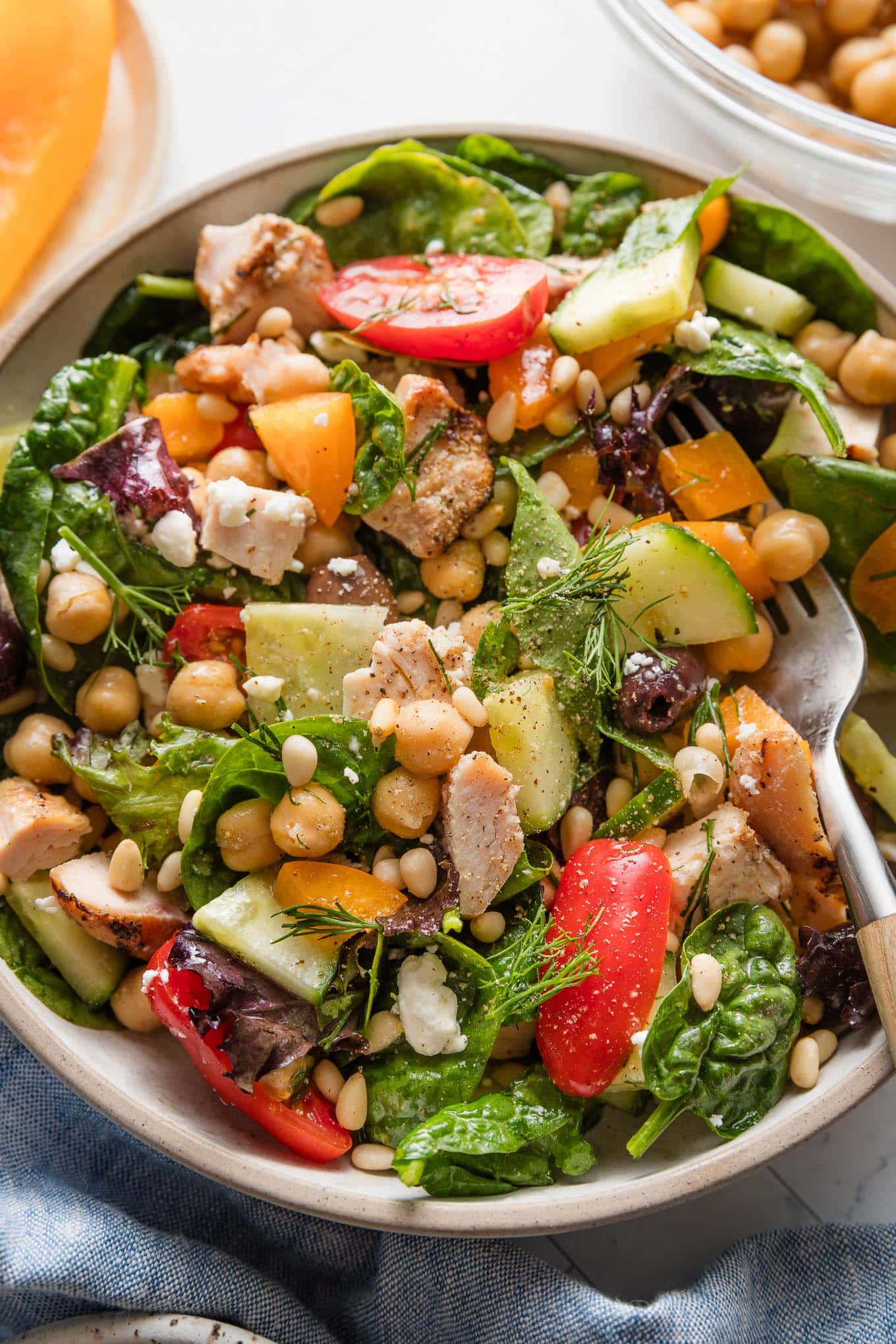 Bowl full of a chopped Mediterranean-style salad with greens, veggies, olives, and grilled chicken.