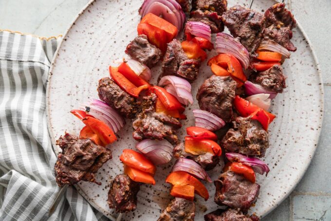 Plate with steak kabobs with pepper and red onion resting on it.
