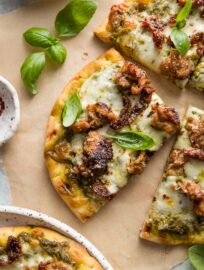 Close up of a slice of pesto sausage flatbread with fresh basil leaves on top as a garnish.