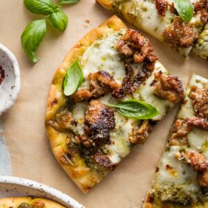 Close up of a slice of pesto sausage flatbread with fresh basil leaves on top as a garnish.