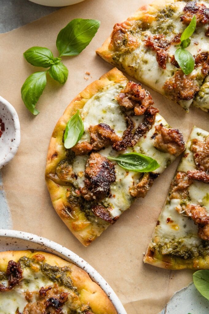 Close up of a slice of pesto sausage flatbread with fresh basil leaves on top as a garnish.