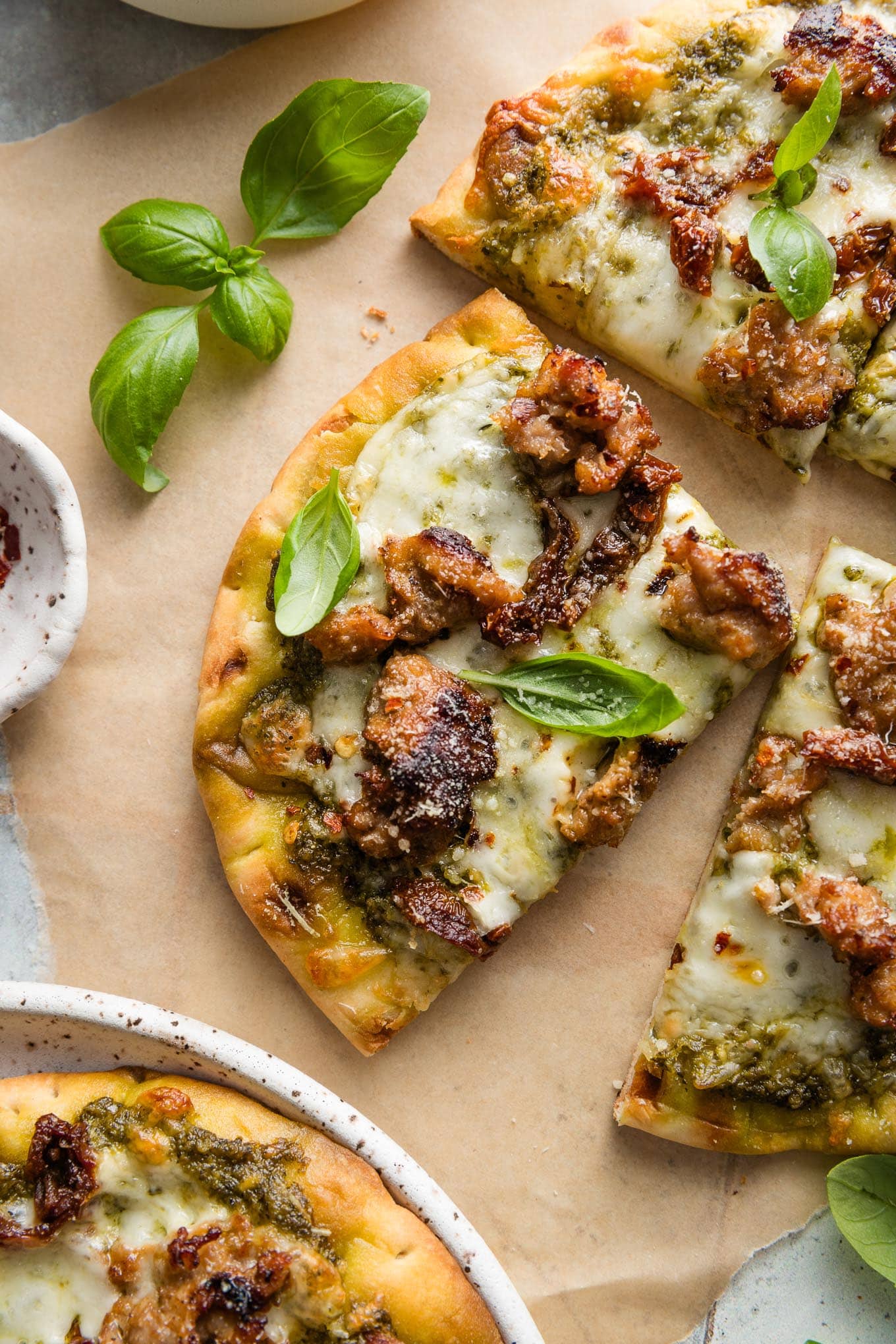 Close up of a slice of pesto sausage flatbread with fresh basil leaves on top as a garnish.
