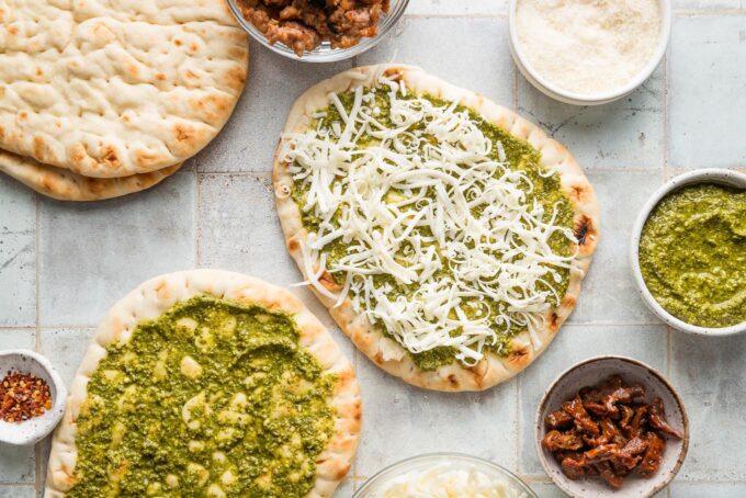 Flatbread pizza topped with basil pesto and shredded mozzarella cheese.