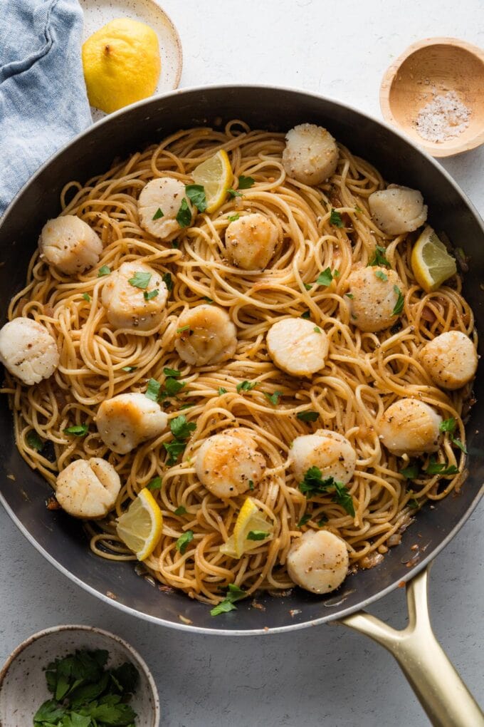 Large skillet filled with a dish of quick pan-seared scallops with pasta, parsley, and lemon.