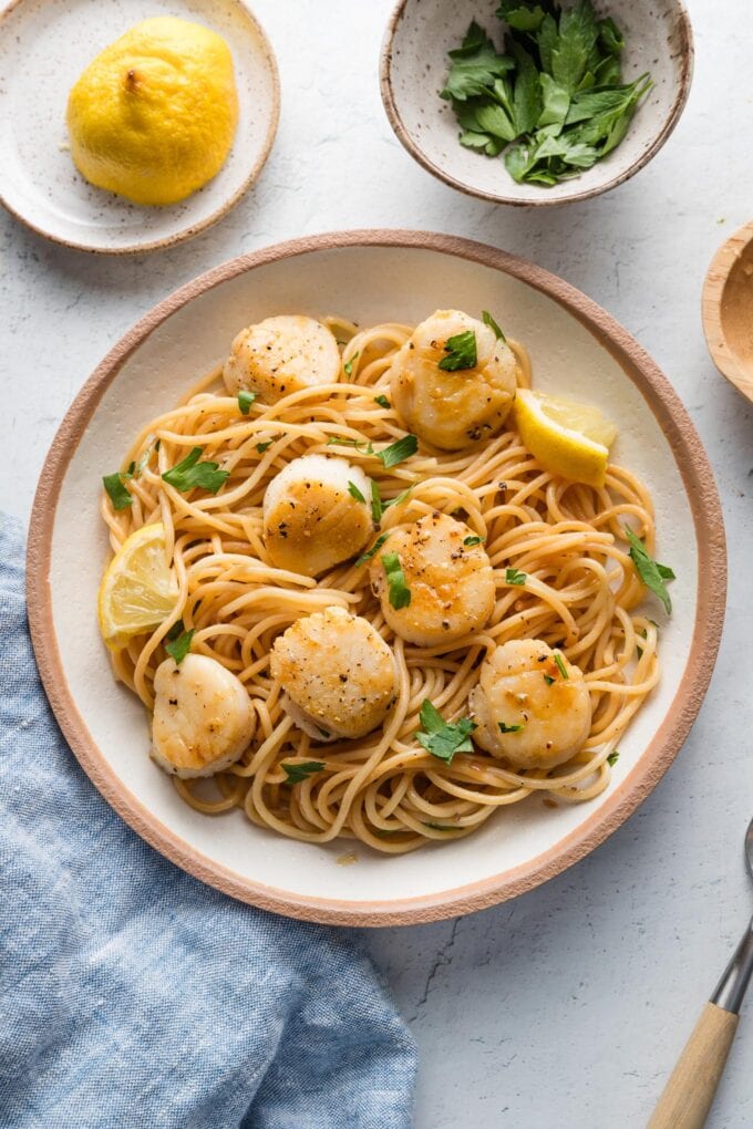 Countertop set with a bowl of scallops with pasta and extra fresh parsley and lemon for a garnish at the table.