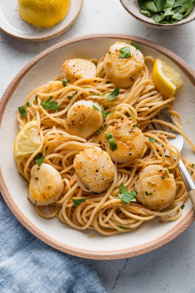 Bowl of spaghetti with pan-seared scallops, a butter shallot sauce, lemon wedges and parsley.