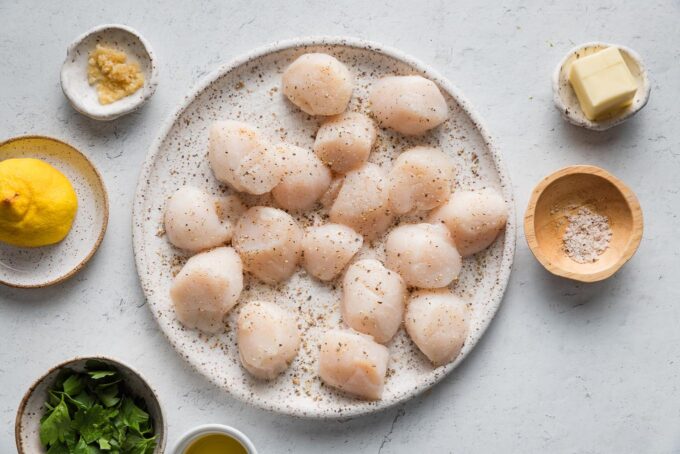 Raw scallops sprinkled with kosher salt and black pepper.