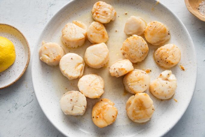 Pan-seared scallops resting on a small white plate.