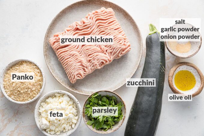Labeled overhead photo of ground chicken, a small zucchini, fresh parsley, crumbled feta cheese, Panko, and seasonings.
