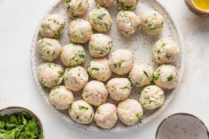 Zucchini chicken meatballs rolled smooth and resting on a plate, ready to cook.