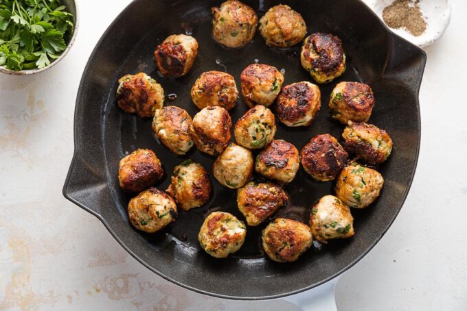 Deeply browned chicken zucchini meatballs in a cast iron skillet.
