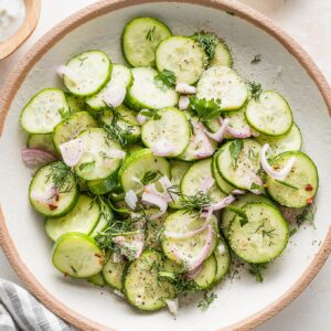 Small bowl full of a cucumber shallot salad with fresh dill and a light white wine vinegar and honey based marinade.