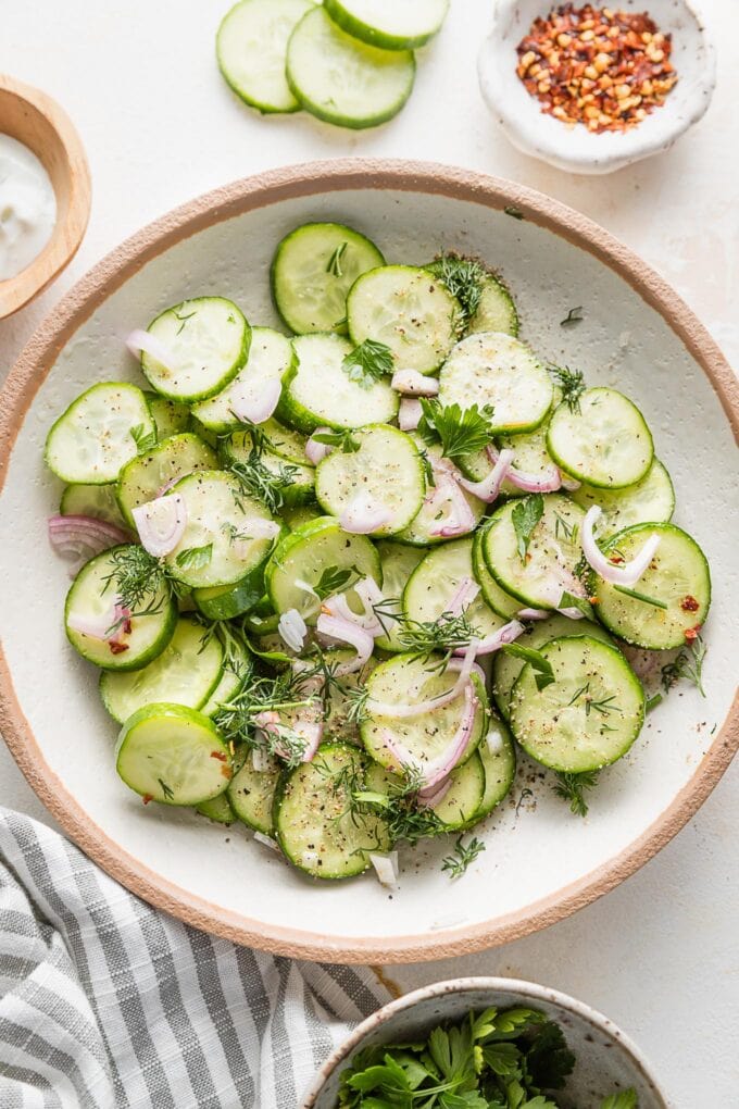 Small bowl full of a cucumber shallot salad with fresh dill and a light white wine vinegar and honey based marinade.