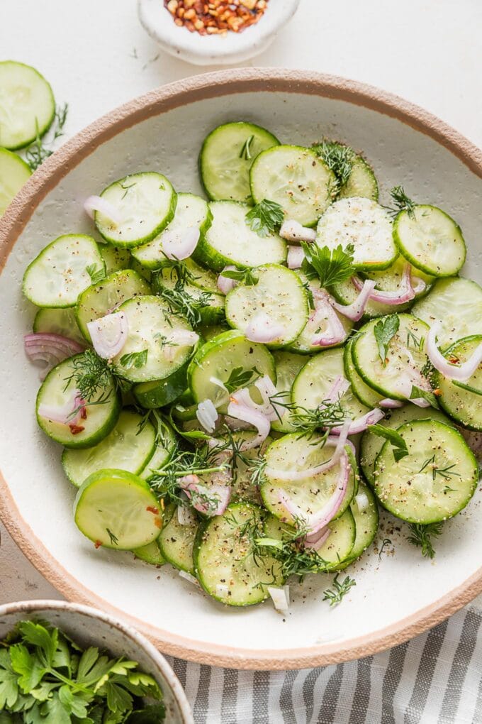 Close up of a cucumber shallot salad served with fresh dill and cracked black pepper on top.