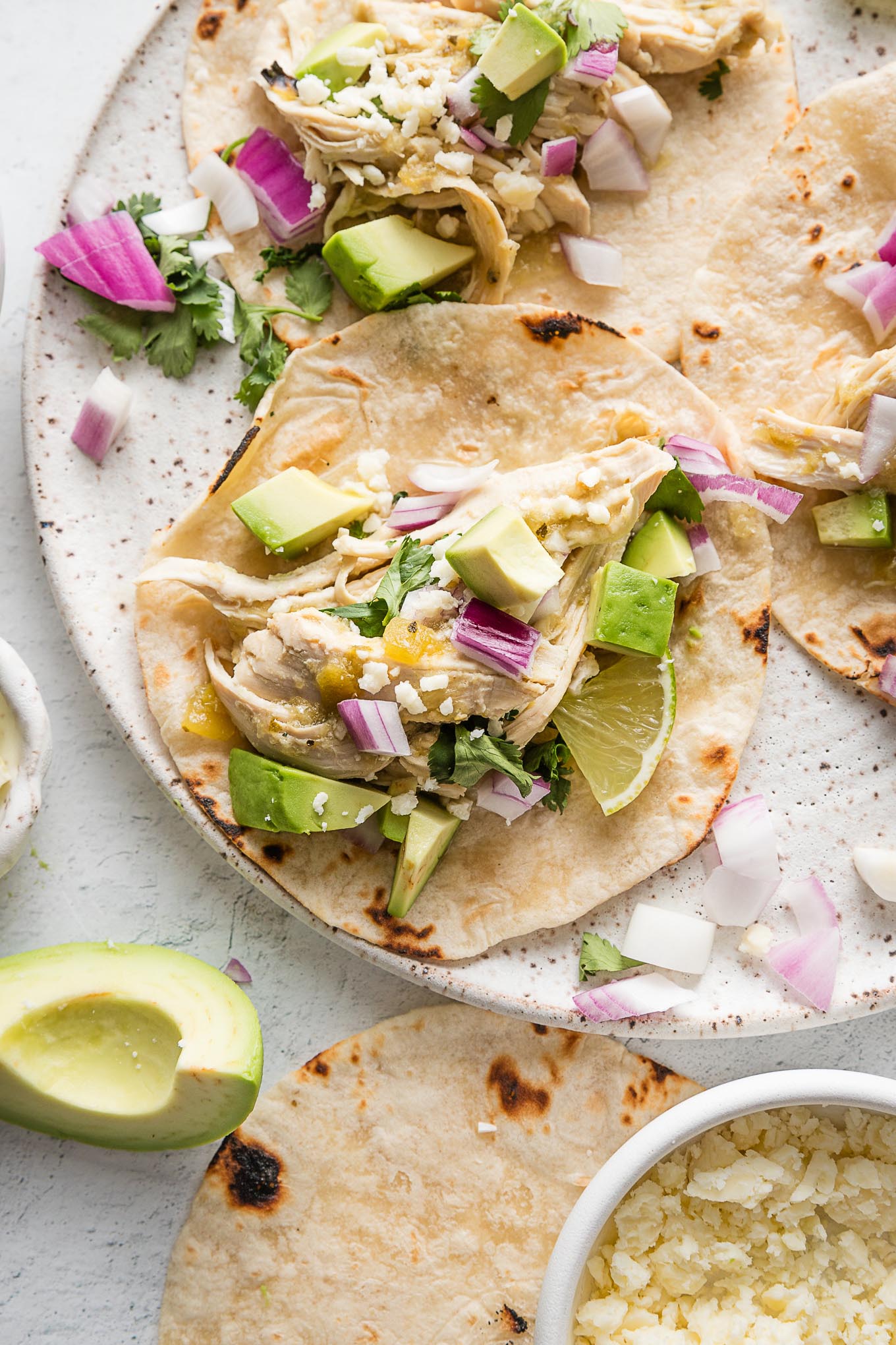 Plate full of slow cooker salsa verde chicken tacos with avocado, lime wedges, cilantro, and Cotija.