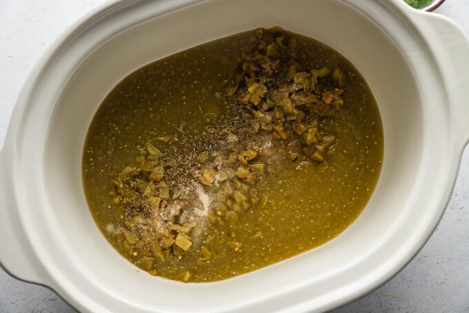 Large slow cooker bowl full of salsa verde, mild green chiles, and spices.
