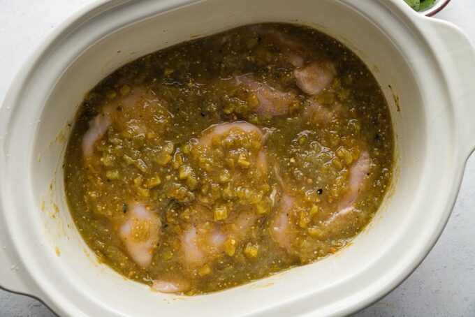 Uncooked chicken breasts added to a slow cooker and coated with a salsa verde sauce.