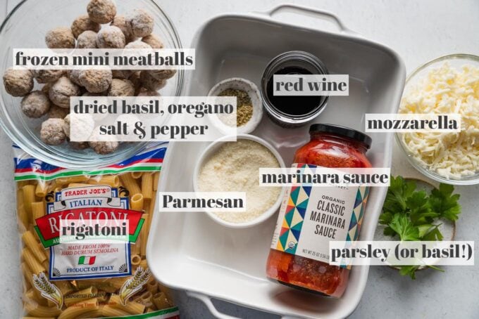 Labeled overhead photo of dried rigatoni, marinara sauce, frozen miniature meatballs, mozzarella and Parmesan cheese, red wine, and seasonings.