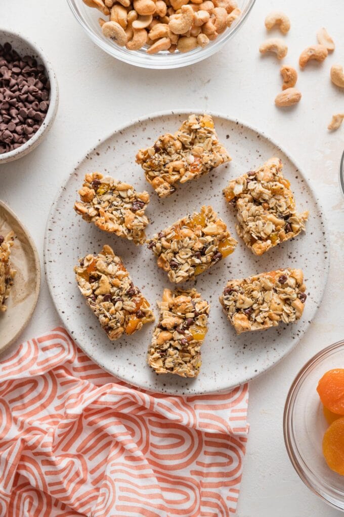 Countertop set with a plate of homemade snack bars made with old-fashioned oats, honey, chia seeds, cashews, dried apricots, and mini chocolate chips.